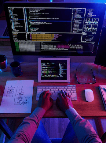 Image of person coding on a laptop computer with large monitor