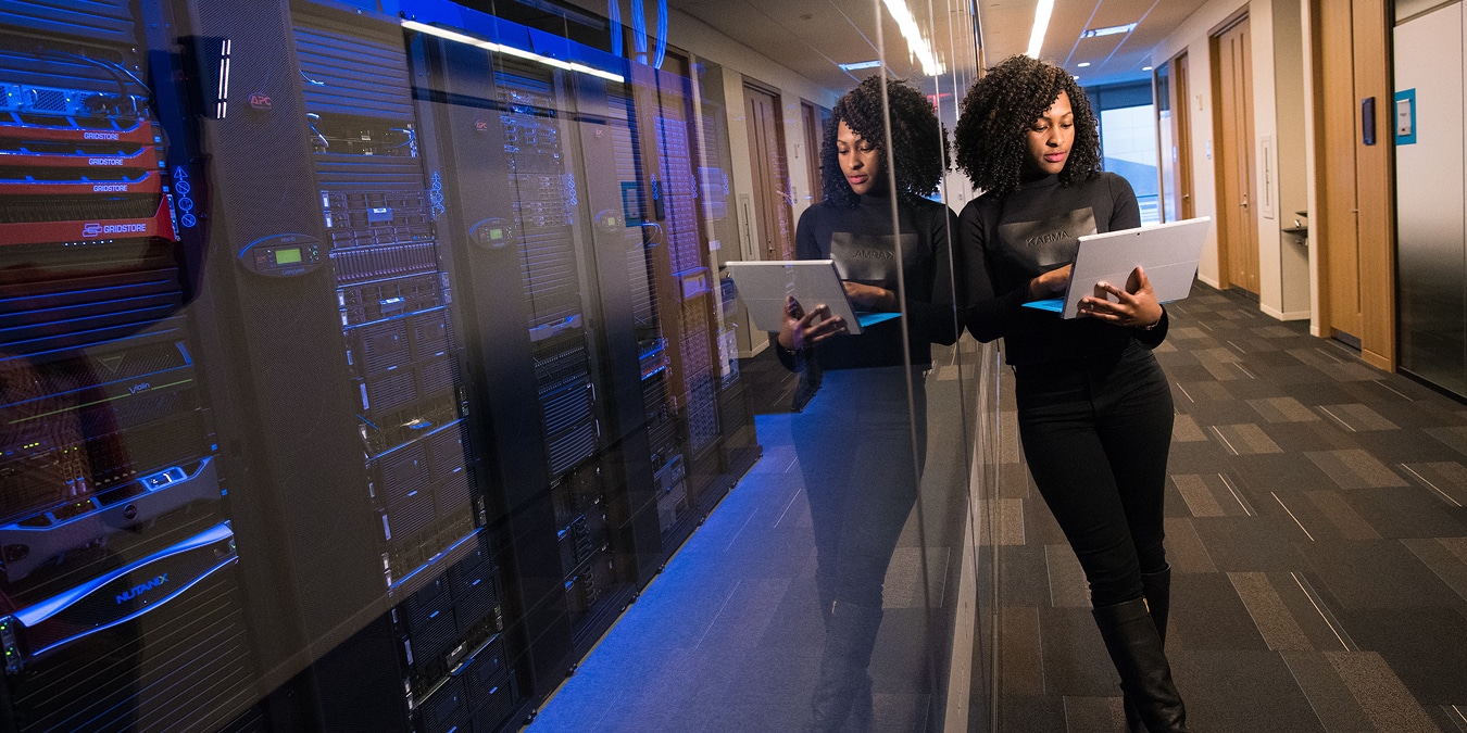 Woman working on laptop in front of rows of servers